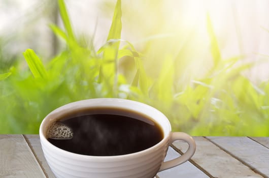 Black coffee in white cup on wood table with garden background. With copy space for text or design.