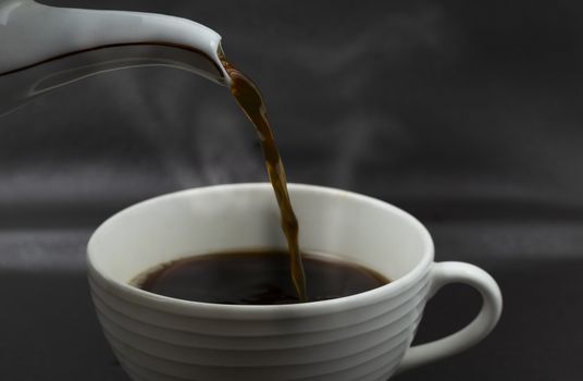Close up pouring the black coffee from pot into cup