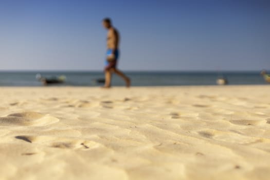 Holiday concept. Clear sand with blur guy, sea and clear sky background. Soft focus and focus selective sand.