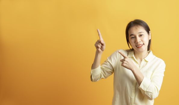 Beautiful smiling Asian woman show pointing two hand to empty space aside studio shot on yellow background with copy space. Asian women with two hand pointing isolated on yellow backdrop.