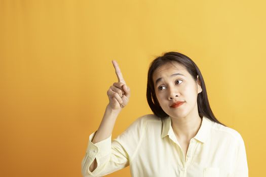 Beautiful smiling Asian woman show pointing  hand to empty space aside studio shot on yellow background with copy space. Asian women with hand pointing isolated on yellow backdrop.
