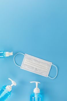 Top view medical face mask and  3 Different  bottle alcohol gel on light blue background with copy space. Face mask and hand sanitizer gel in pump head bottle.