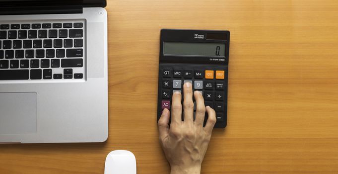 Top view women hand using calculator on office desk. Female hand press calculator. Business woman hand using calculator at office. Family budget calculation on wood table.