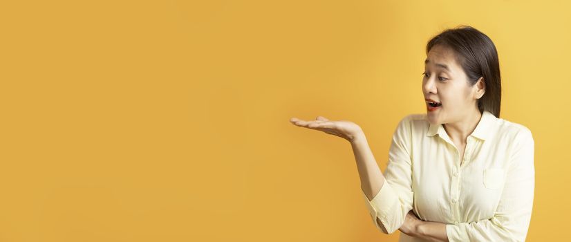 Beautiful Asian women showing open hand palm and looking sideway on yellow background with copy space.