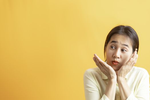 Asian women surprised happy looking sideways in excitement on yellow background with copy space.  asian women take two hand holding her face.