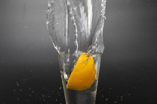 Orange slice falling and dropping into a splashing glass with black background.