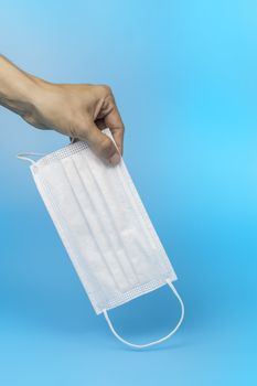 Women hand pickup and hold medical face mask on blue background. Women hand hold medical protective mask on blue background with copy space.