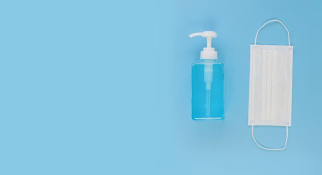 Top view medical face mask and alcohol gel on light blue background with copy space. Face mask and hand sanitizer gel in pump head bottle.
