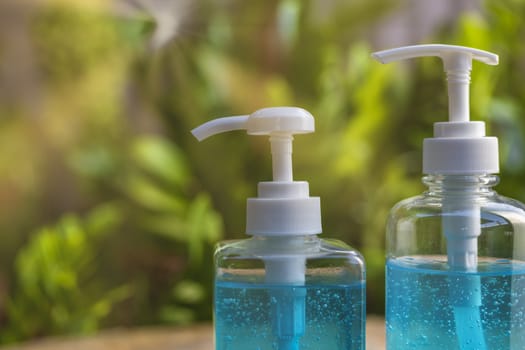 Blue alcohols gel bottle on blur green nature background and sun ray. Hand sanitizer gel in pump bottle. With copy space for text or design. Blue alcohols gel on wood table. Alcohols gel in 2 different size pump bottle. 