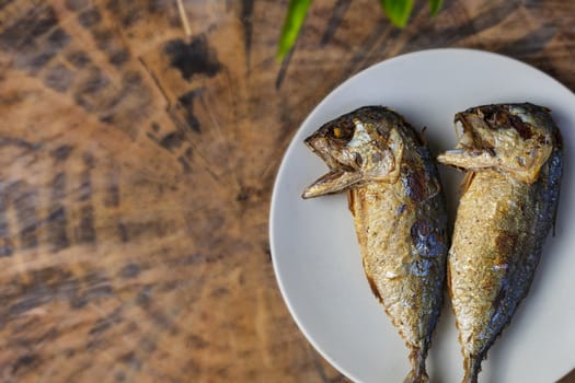 Top view fried mackerel on a white plate with real wooden table with copy space for text or design. Fried fish on the dish.