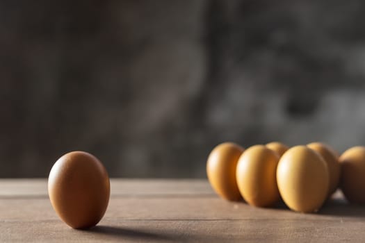 social distancing concept. Checken eggs have one chicken egg is far away from the group of chicken eggs.
Interpret social distancing. One and group for chicken eggs on wood table with copy space for text or design.Soft focus and focus selective alone egg.