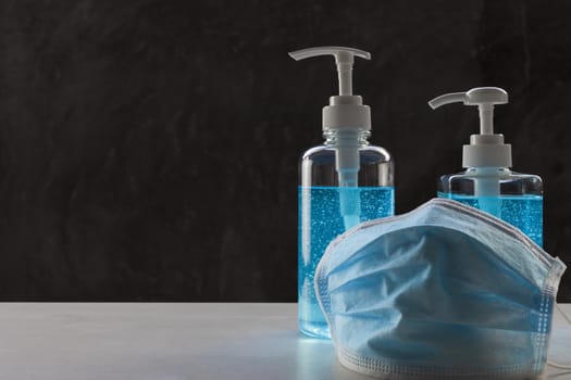 Face mask with alcohol sanitizer gel hand wash on wood table and raw cement background with copyspace for text or design.
