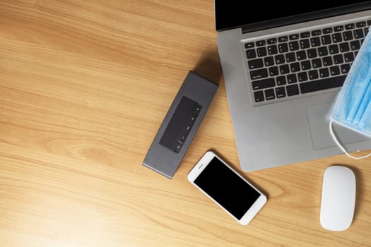 Work from home concept. Top view laptop, mouse, smartphone, speaker and face mask on wood table with copyspace for text or design.