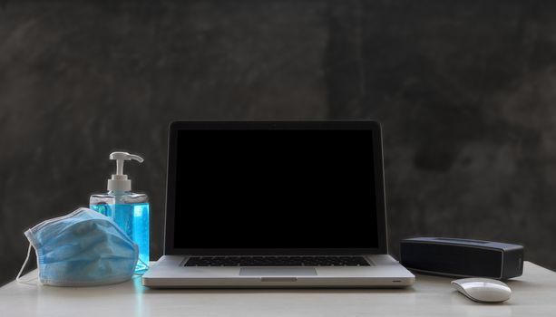 Laptop, mouse, speaker, alcohols gel and Medical mask on white wood table and  raw cement  background with copyspace for text or design.