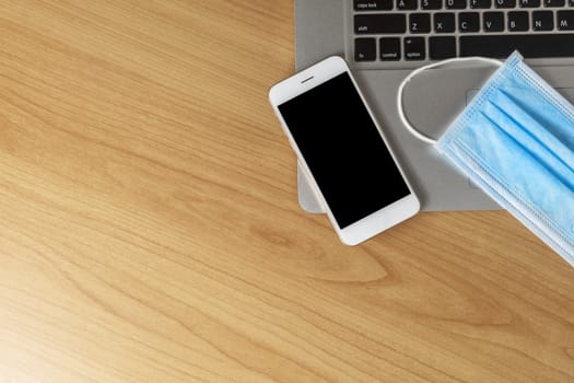 Work from home concept. Top view laptop, smartphone, and face mask on wood table with copyspace for text or design.