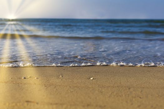 Soft wave from sea come to wet sand beach with blur clear sky and sun ray background. With copy space for text or design. Beach background.