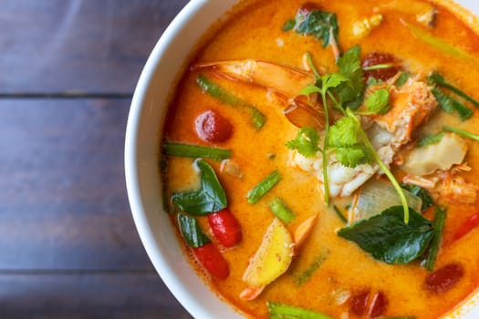 Top view Tom Yam kung Spicy Thai soup with shrimp in white bowl on wood table. With copy space for text or design.