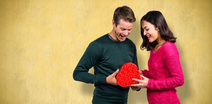 Happy young couple with heart shape gift against orange background 