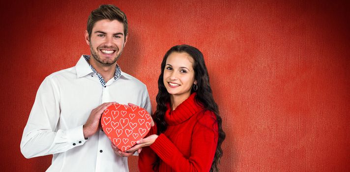 Couple holding heart shaped gift box against red background