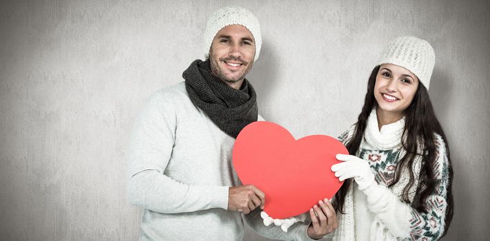 Smiling couple holding paper heart against white and grey background