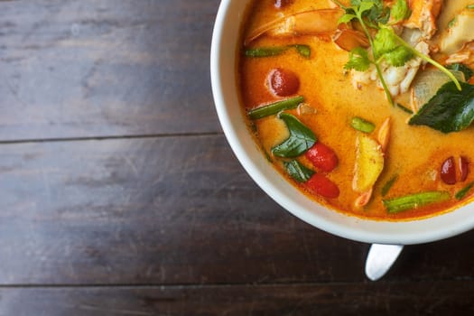 top view Tom Yam kung Spicy Thai soup with shrimp in white bowl on wood table. With copy space for text or design.