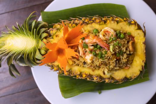 Top view Thai royal pineapple fried rice. Fried rice with shrimps served in a pineapple on wood table.