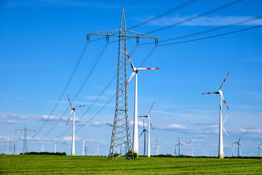 Overhead power lines and wind engines on a sunny day seen in Germany