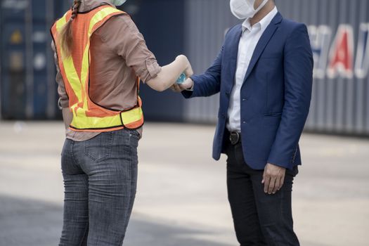 Factory woman worker in a face medical mask and safety dress using alcohol gel for hand cleaning to protect coronavirus disease at outdoor factory warehouse at worker people standing on queue. Background of cargo container warehouse.
