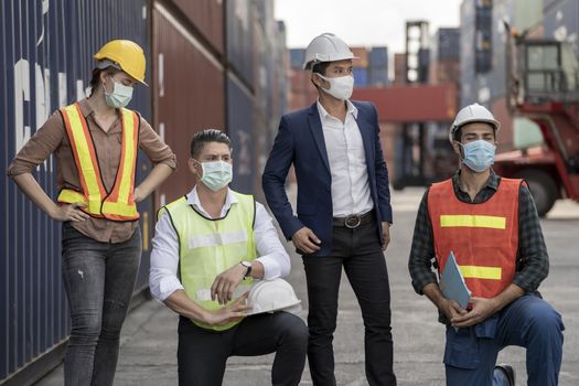 group people worker is wearing protection mask face and safety helmet and wearing suit safety dress With background of container cargo warehouse. Concept of industry worker operating.