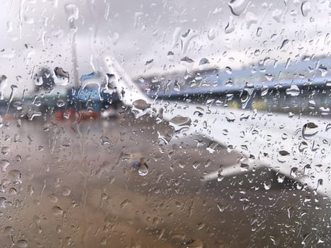 On a rainy day windows of the aircraft were filled with rain and blurred aircraft in the aircraft parking.