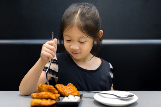 Hungry Asian kid eating fried chicken at restaurant.