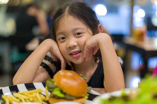 Hungry Asian child eating hamburger at restaurant.