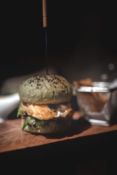 Burger and fries on wooden plate with black background.