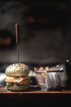 Burger and fries on wooden plate with black background.