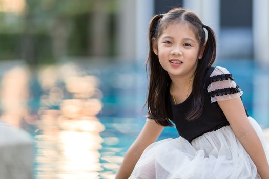Asian kid smiling at outdoor swimming pool.