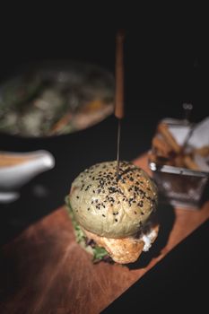Burger and fries on wooden plate with black background.
