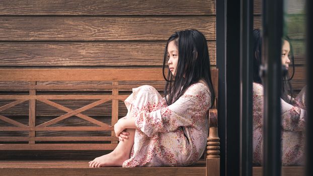 Asian kid sitting next to window alone with sadness.