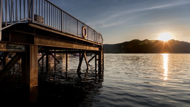 Sunset or sunrise scene of dock at lake and mountain.