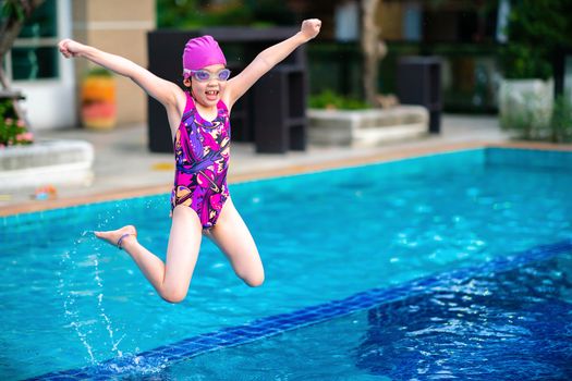 Little girl, kid, jumping into swimming pool with happiness and fun.