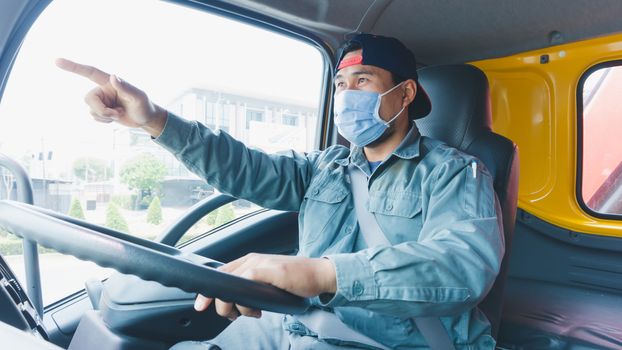 Close-up photos of Asian truck drivers wearing masks to protect against dust and the spread of the flu. Covid 19. Inside the car front.He is smiling and pointing forward.