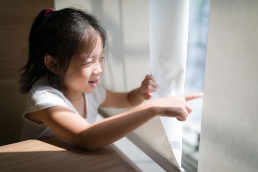 Concept of exploring illustrated by Asian child pointing out and looking out window.