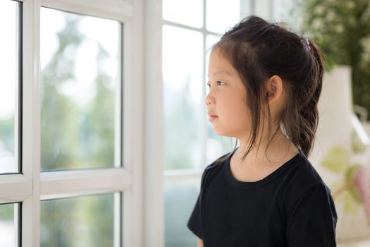 Lonely Asian child looking out window expressing her emotion.