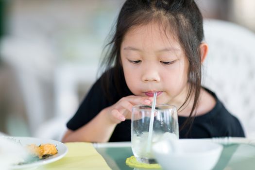 Asian child drinking water using straw from glass when having dinner.