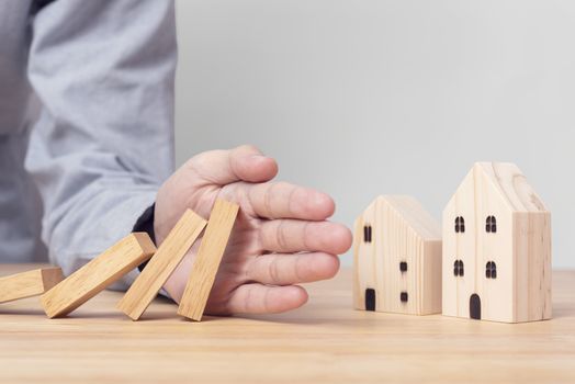 Hand stopping wooden block domino with home. concept home insurance.