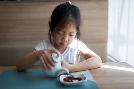 Little Asian child pouring soy sauce.