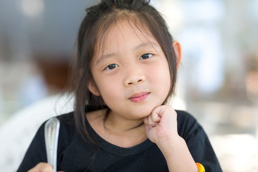 Cute Asian child holding spoon at restaurant.