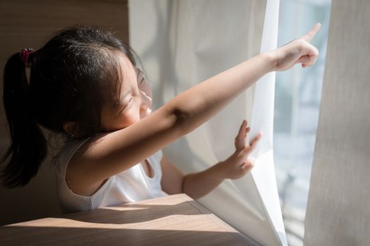 Concept of exploring illustrated by Asian child pointing out and looking out window.