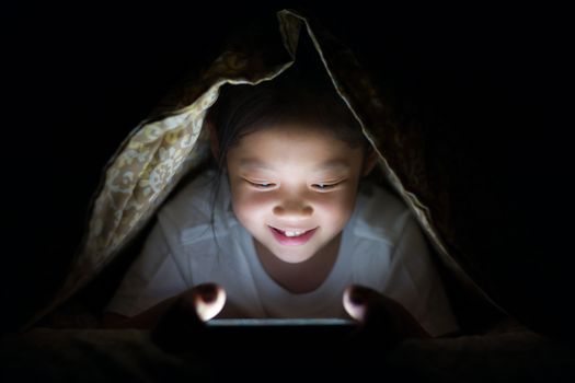 Happy Asian child using on tablet PC in her bed at night.