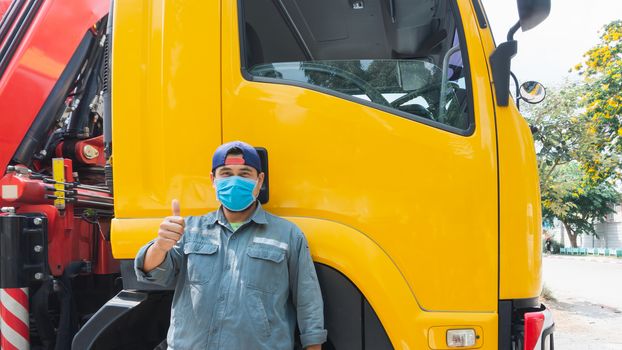 The truck driver, an Asian man, was standing at the door of the car. He put on a mask to prevent dust and prevent the spread of the virus.