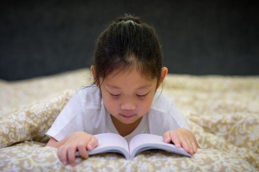 Asian child reading book in her bed.